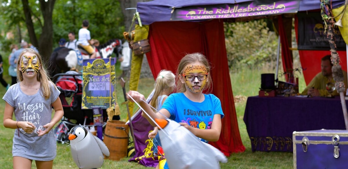 Street fair guests watch in awe as NYX the Jester and Clyde P. Riddlesbrood perform an interactive Trunk Show act.