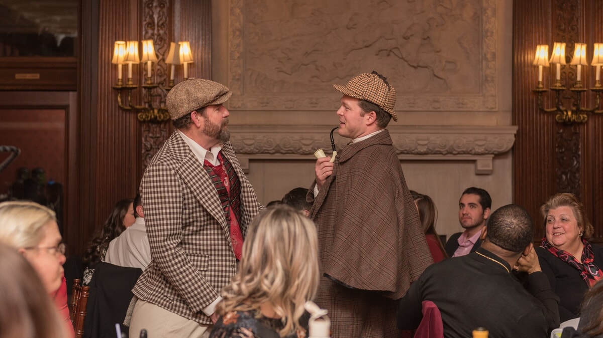 A Sherlock Holmes actor inspects a crime scene with a magnifying glass, showcasing the consistent quality of an immersive murder mystery experience.